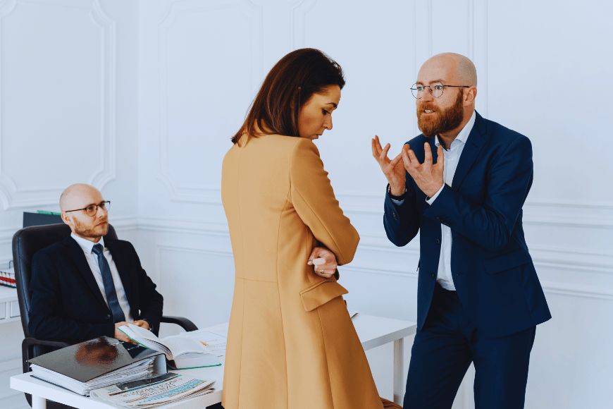 Workplace conflict scenario showing a man speaking aggressively to a colleague while another employee observes, illustrating bullying behaviour at work.